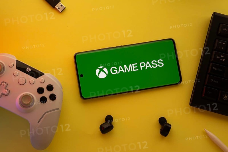Dhaka, Bangladesh- 15 July 2025: Smartphone with Xbox game pass logo, game controller, and earbuds on a yellow background