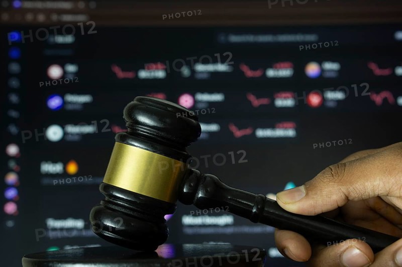 Dhaka, Bangladesh- 20 June 2025: A hand holds a gavel in front of a computer screen displaying Kraken's website