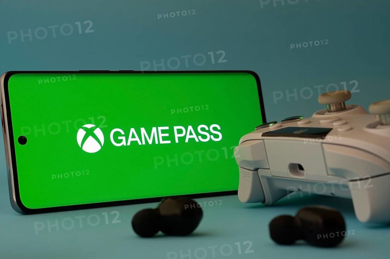Dhaka, Bangladesh- 15 July 2025: A smartphone with a Xbox Game Pass icon next to a controller and earbuds on a blue surface