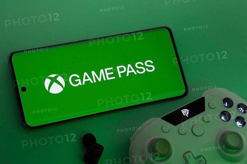 Dhaka, Bangladesh- 15 July 2025: Smartphone with Xbox Game Pass logo, game controller, and earbuds on a green background