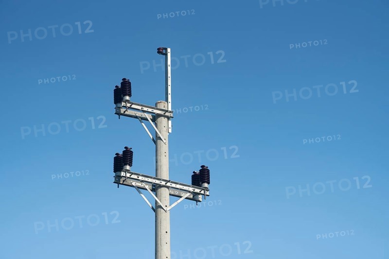 An electric pole with insulators and wires set against a clear blue sky on a bright day