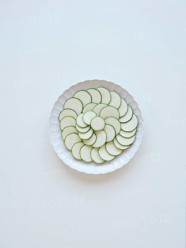 Thinly sliced zucchini arranged on a white plate, forming a visually appealing pattern of concentric circles