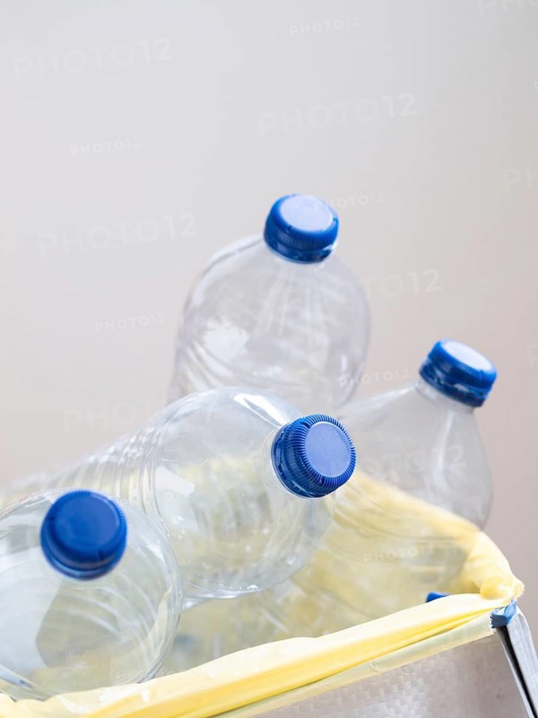 Empty plastic bottles with blue caps are being thrown away in trash can for recycling