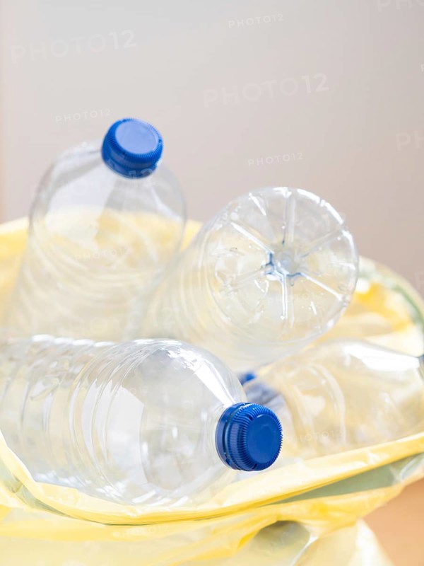 Close-up of empty plastic bottles with blue caps, placed inside a yellow recycling bag, promoting environmental awareness