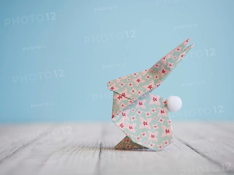Floral origami easter bunny standing on a wooden table against a blue background