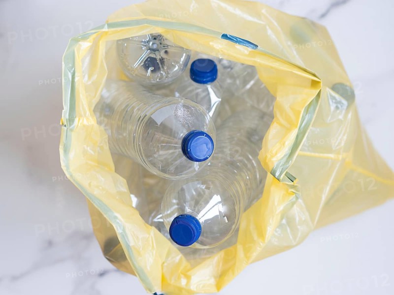 Plastic bottles with blue caps collected in yellow trash bag ready for recycling