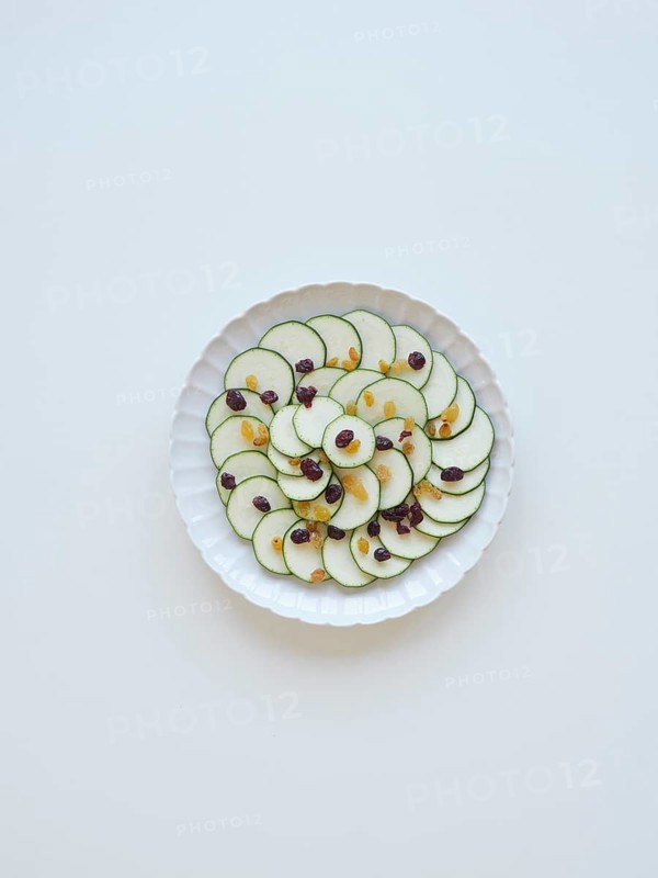 Thinly sliced zucchini arranged on a white plate, garnished with raisins and cranberries, creating a visually appealing and healthy dish