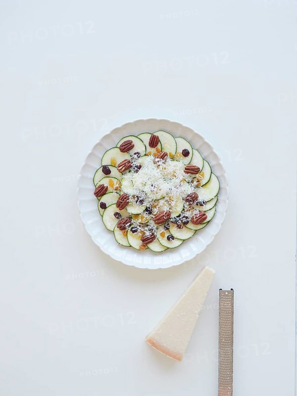 Delicious zucchini carpaccio with parmesan cheese, pecan nuts, raisins and cranberries served on white plate