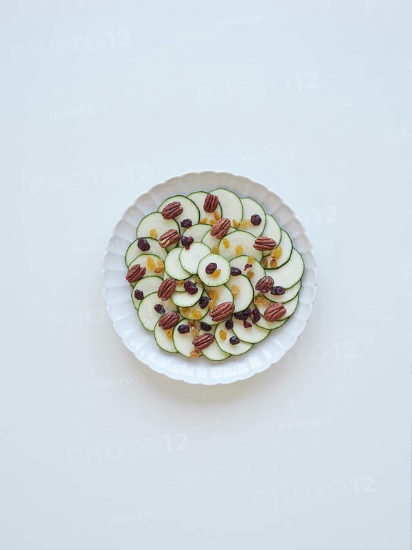 Sliced zucchini arranged on a white plate, creating a carpaccio with raisins and pecans, forming a healthy and visually appealing dish