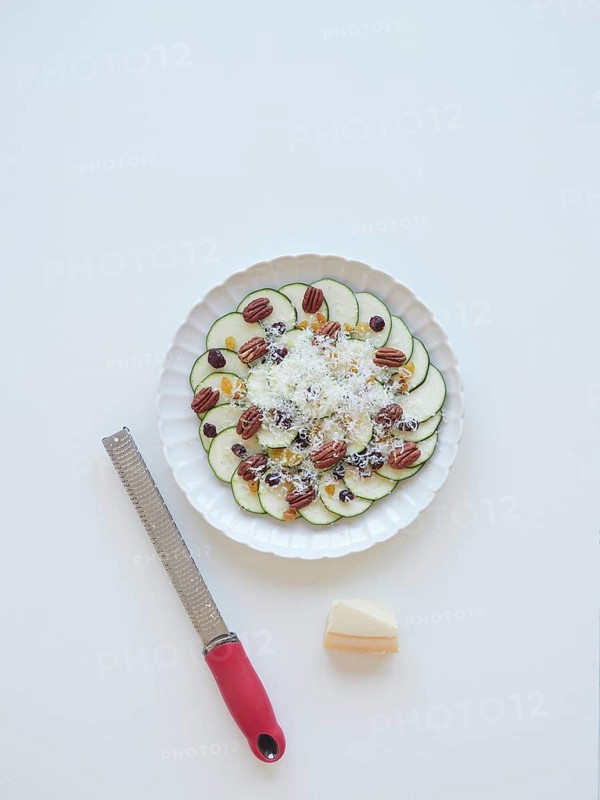 Delicious zucchini carpaccio with parmesan, pecan nuts, raisins, and grater on a white background, ready to be enjoyed