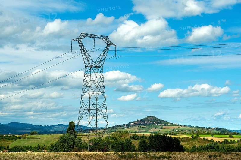 High voltage power lines against a bright blue sky with scattered clouds, Puy de Dome, Auvergne Rhone Alpes, France