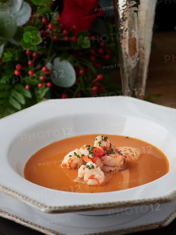 Creamy shrimp bisque soup with prawns, garnished with chives, on a white plate