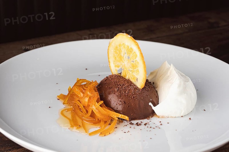 Chocolate mousse dessert with candied orange peel, dried orange slice, and cream on a white plate