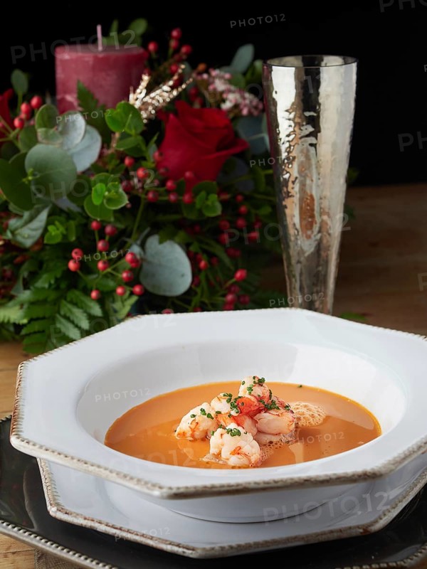 Shrimp bisque serving with prawns, chives, and foam, featuring a festive table setting