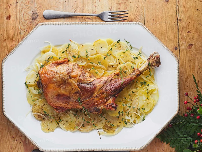 Whole roast leg of lamb with thinly sliced potatoes, onions, and fresh thyme sprigs