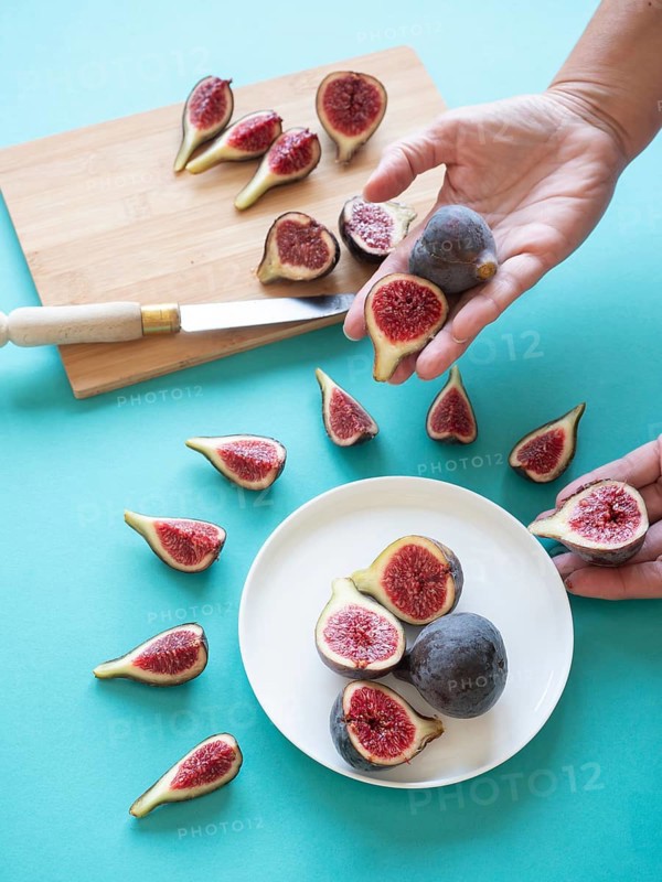 Hands arranging fresh, cut figs on a white plate and cutting board