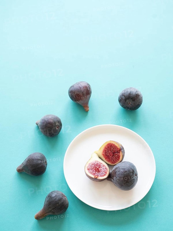 Ripe figs arranged on a white plate and scattered on a blue surface