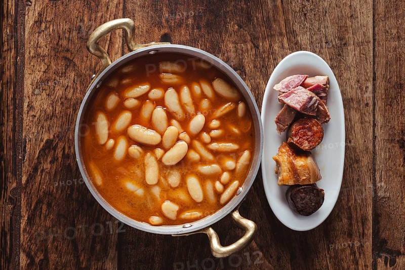 Fabada, a traditional asturian bean and pork stew, serving on a wooden table
