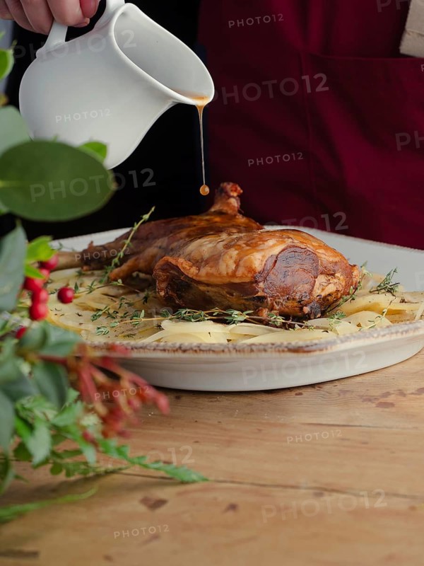 Hand pouring gravy from a pitcher onto a roasted lamb leg