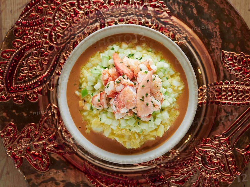 Gourmet lobster gazpacho with diced cucumber and chives, presented on an ornate platter