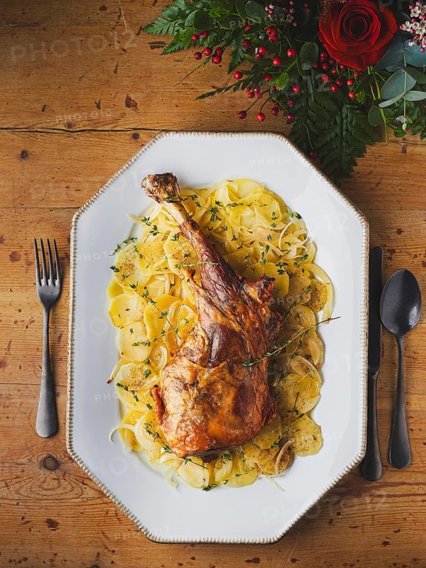 Roasted leg of lamb serving with sliced potatoes and fresh thyme on a wooden table