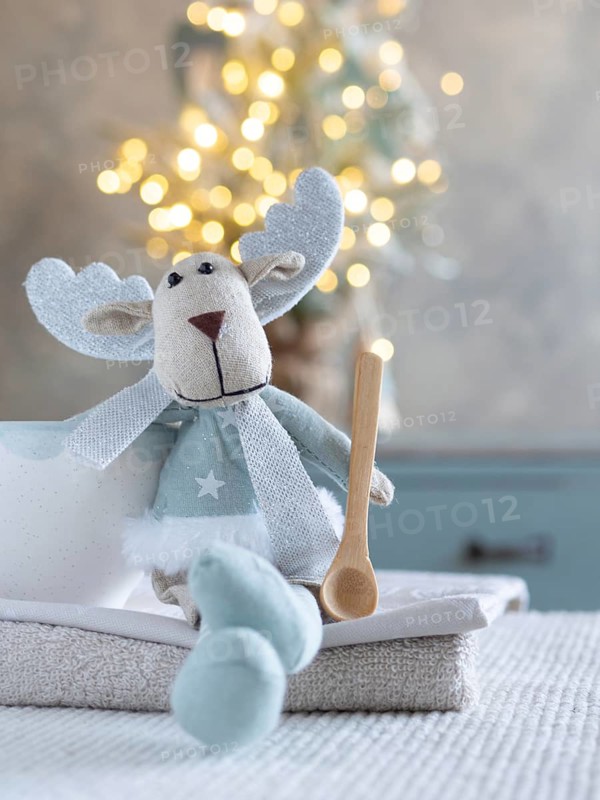 Fabric reindeer toy sitting with a wooden spoon and cozy christmas lights