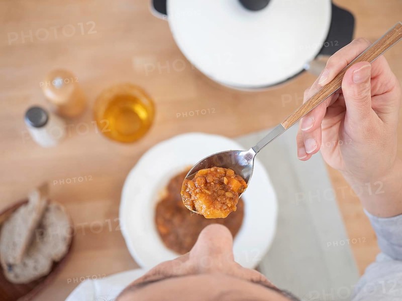 Woman holding a spoonful of lentil stew at lunch, top view of the table