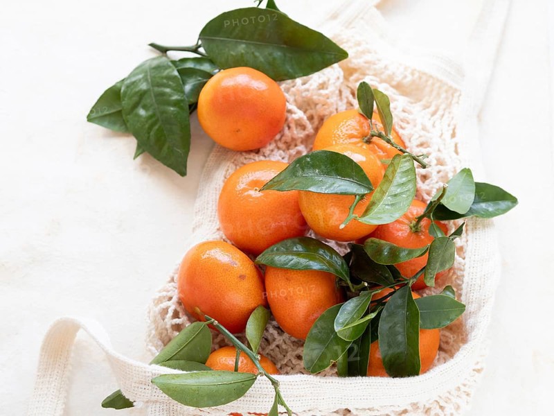 Vibrant tangerines with green leaves rest in a reusable shopping bag, embodying eco-conscious consumerism and sustainable living