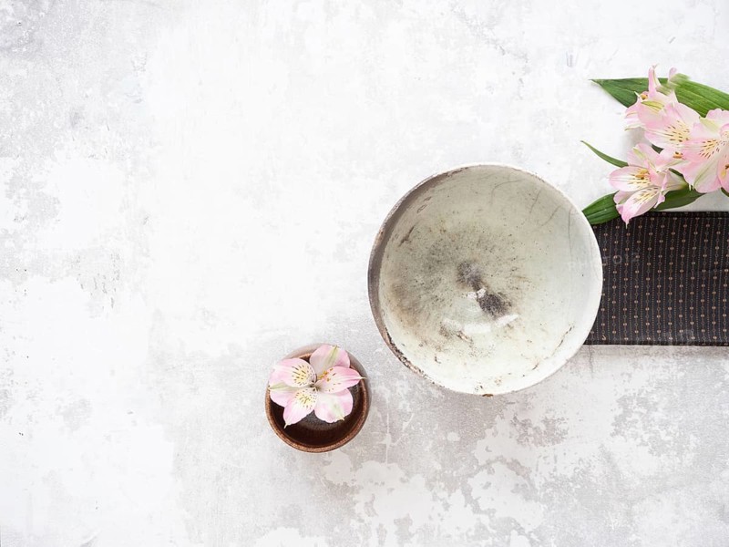 Empty ceramic bowl, pink alstroemeria flowers, and brown placemat creating a minimalist arrangement on textured surface, ideal for food photography or wellness blogs
