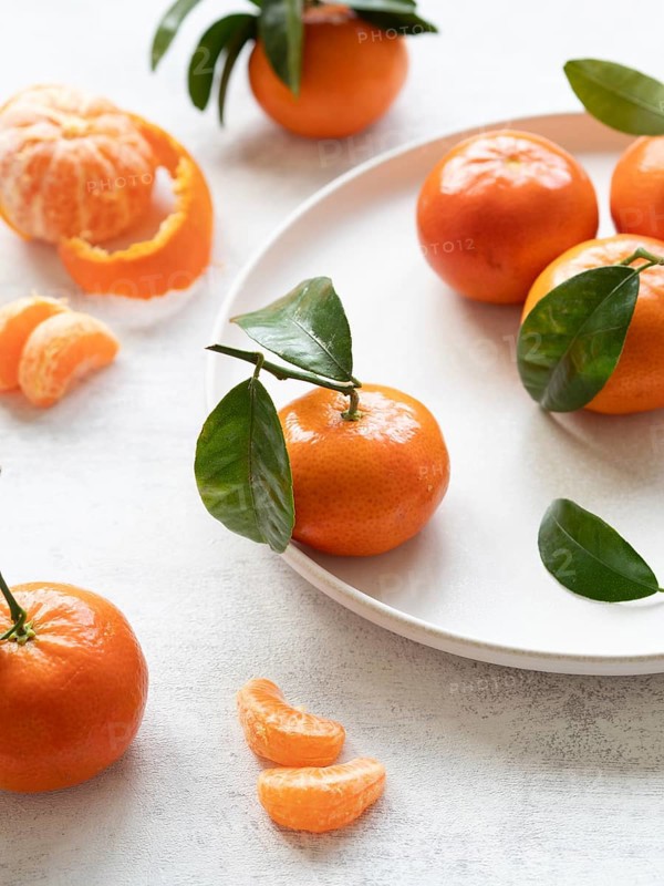 Vibrant tangerines with green leaves, showcasing freshness and citrusy appeal on a white plate and table