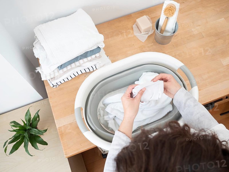 Woman putting clean white clothes into laundry basket, preparing for drying