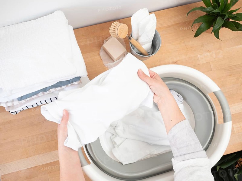 Housewife putting white clothes into basin, doing laundry chores at home