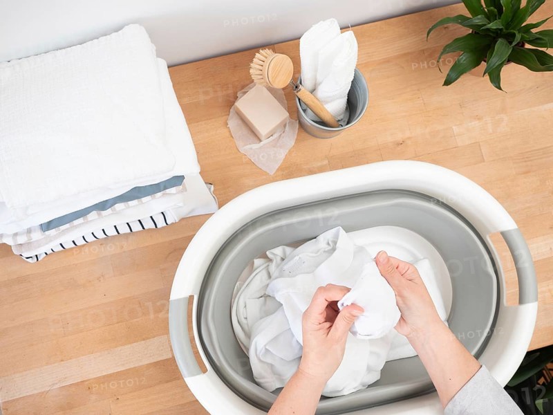 Woman soaking white clothes in bucket using natural soap and brush, promoting sustainable laundry practices