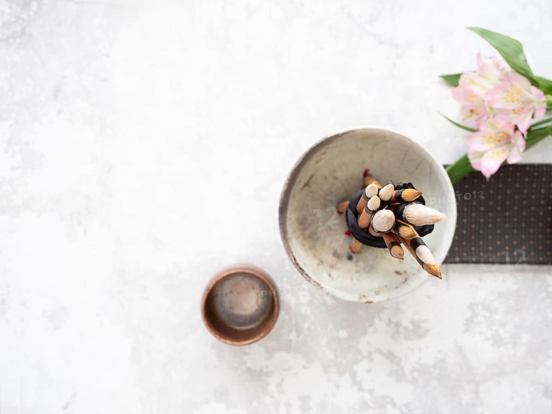 Calligraphy brushes tied with black ribbon in ceramic bowl near inkstone and pink flowers, ready for traditional writing session