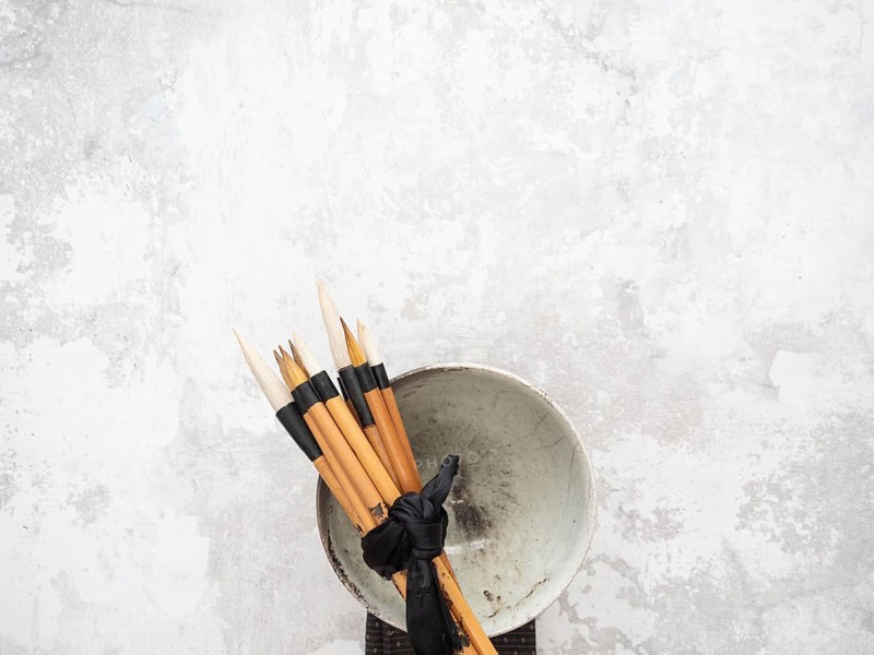 Multiple calligraphy brushes tied together with a black ribbon are resting on a ceramic bowl, evoking traditional art practices