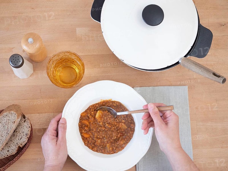 Woman eating a hearty lentil soup with whole grain bread and a glass of beverage, viewed from above