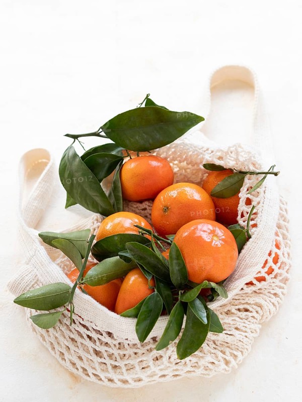 Ripe tangerines with green leaves inside a reusable mesh bag promoting sustainable shopping