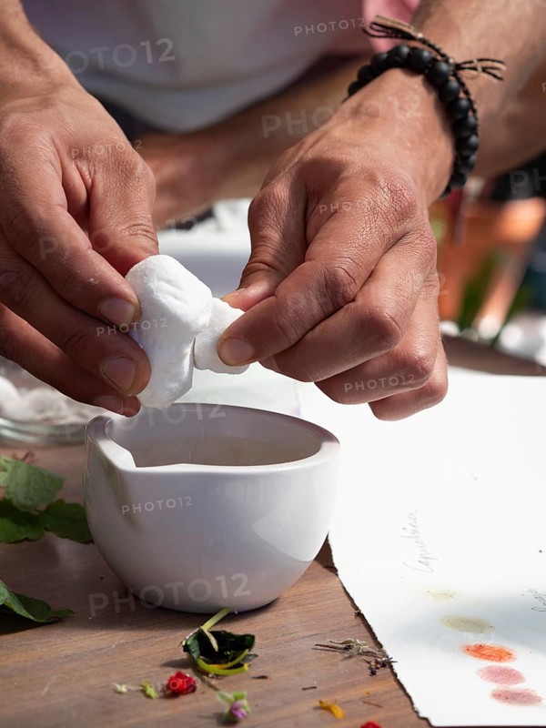 Hands squeezing white flower petals above a mortar for creating natural inks and pigments in a workshop