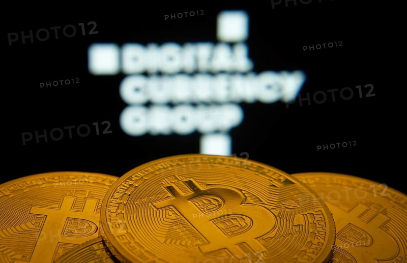 Dhaka, Bangladesh- 03 Oct 2025: Close-up of Bitcoin coins with the Digital currency group logo visible on a screen in the background