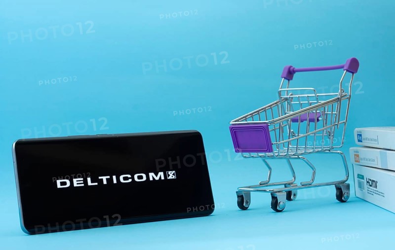 Dhaka, Bangladesh- 03 Oct 2025: Smartphone with Delticom logo next to a small shopping cart and boxes against a blue background