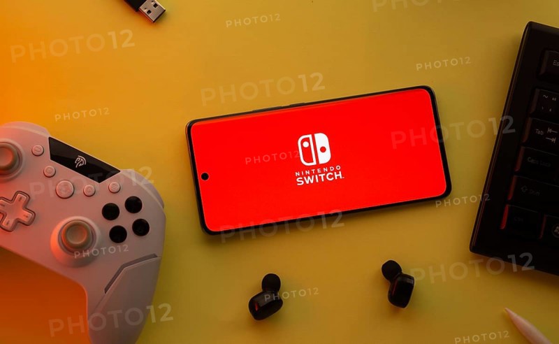 Dhaka, Bangladesh- 15 July 2025: Smartphone with nintendo switch logo, game controller, and earbuds on a yellow background
