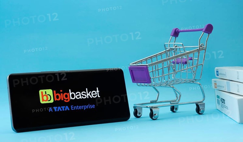 Dhaka, Bangladesh- 03 July 2025: Smartphone with BigBasket logo next to a small shopping cart and boxes against a blue background