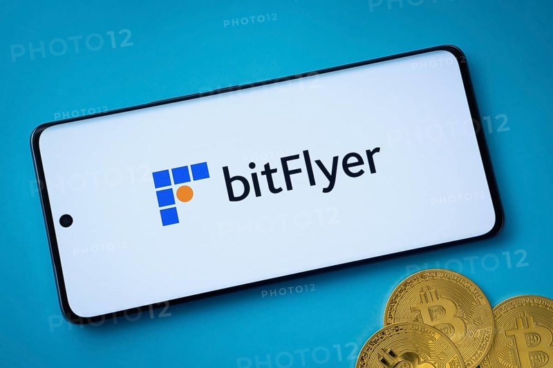 Dhaka, Bangladesh- 02 June 2025: Bitflyer logo on smartphone screen near Bitcoin coin and QR code on blue background