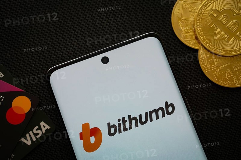 Dhaka, Bangladesh- 07 May 2025: Smartphone displaying Bithumb logo surrounded by Bitcoin coins and payment cards
