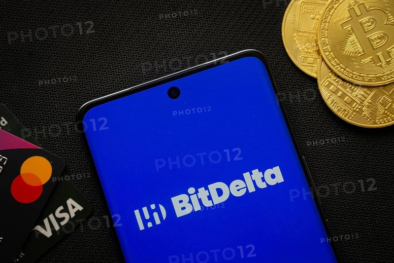 Dhaka, Bangladesh- 02 June 2025: Smartphone displaying BitDelta logo surrounded by Bitcoin coins and payment cards