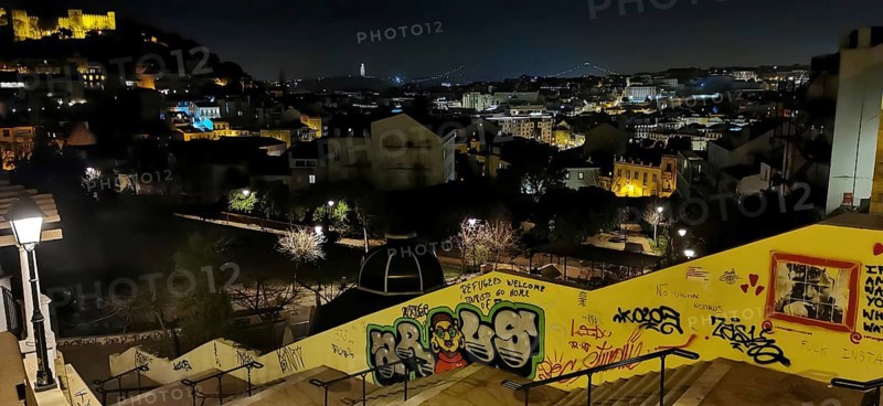 Night view of a long staircase, looking over Lisbon, with illuminated buildings and graffiti on a wall in the foreground, Lisbon, Portugal