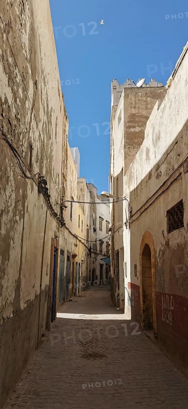 A narrow street lined with old buildings in Essaouira under a deep blue sky in an urban setting, Essaouira, Morocco