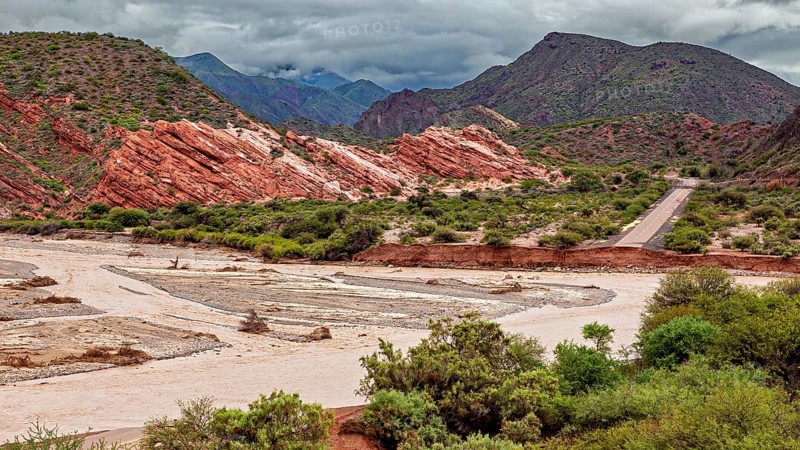 Picturesque valley with road surrounded by red rocks and green vegetation, the landscape and colorful rock formations of the Quebrada de Cafayate near Salta in Argentina
