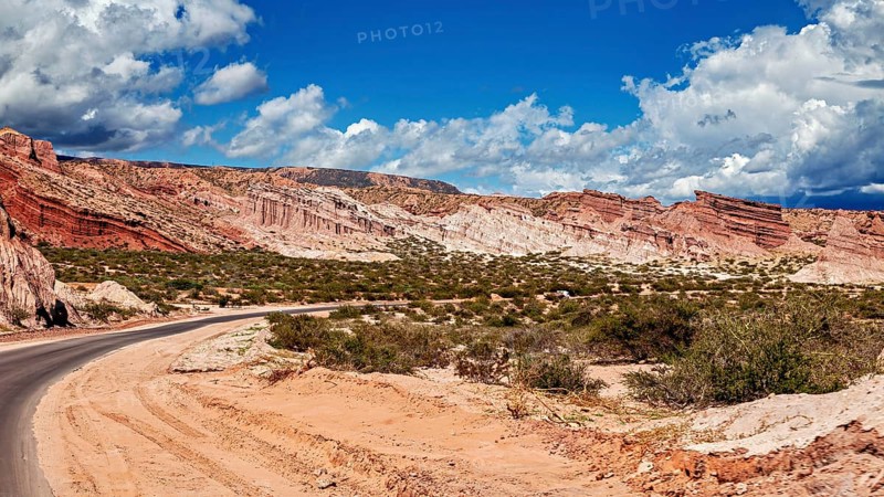 Road snakes through red rocky landscape under a cloudy sky, the landscape and colorful rock formations of Quebrada de Cafayate near Salta in Argentina