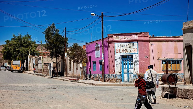 Colourful buildings and people in a bright, dry village with hills in the background, San Antonio de los Cobres, Salta Province, Argentina